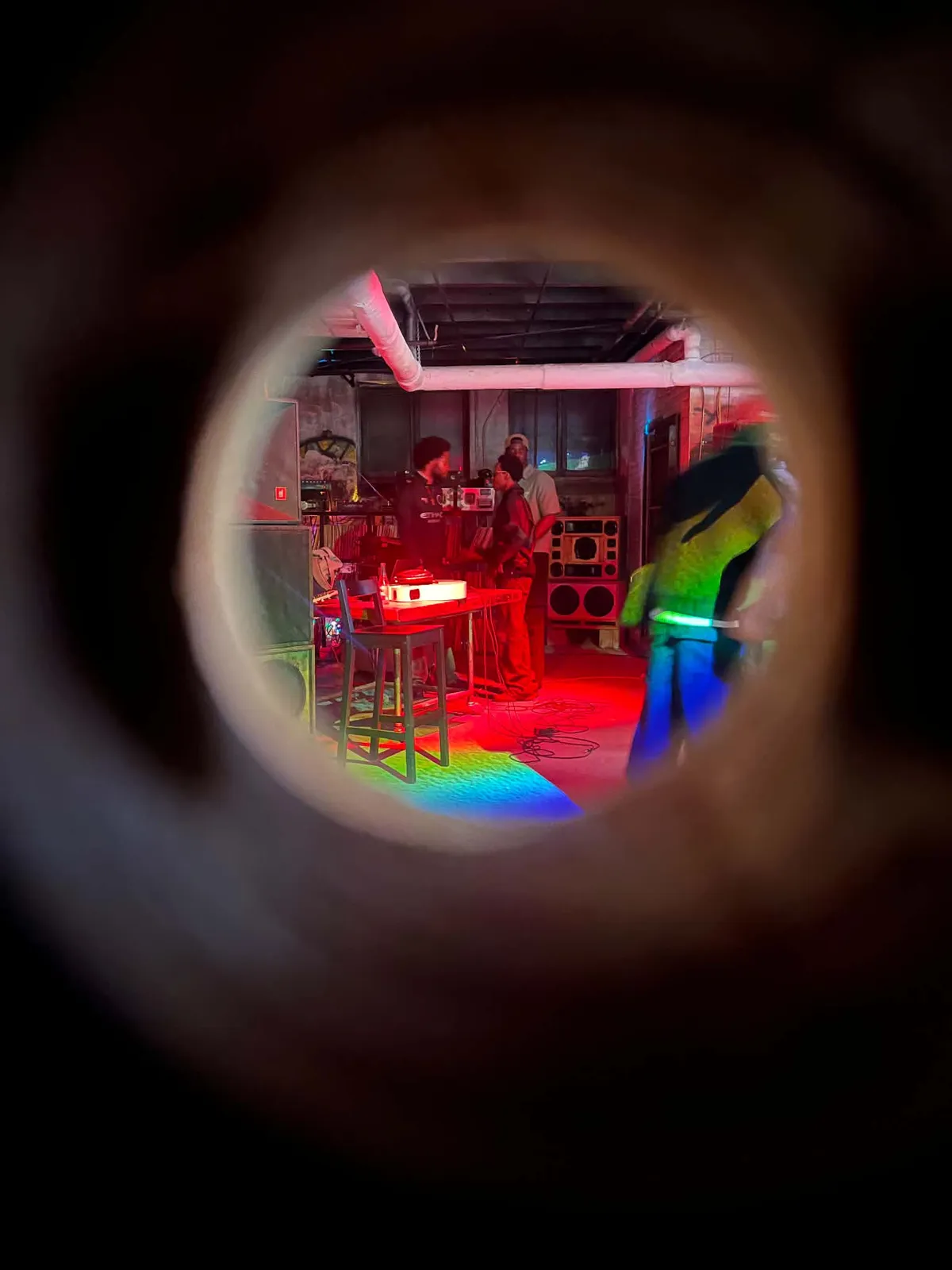 The room seen through a circular lens, red stage light and a scatter of rainbow refraction across the floor.